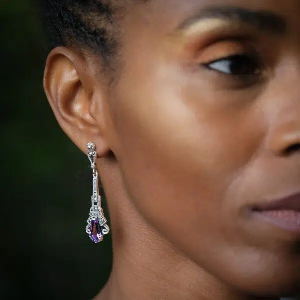 Vintage-style art deco amethyst earrings worn by a model on a black background.