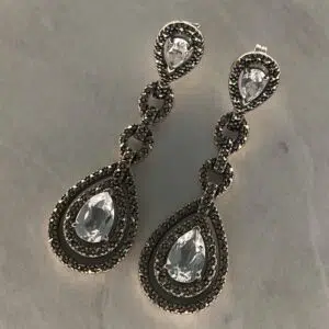 Boucles d'oreilles en argent pendantes sertis de topaze clair et de marcassite posées sur une table grise.