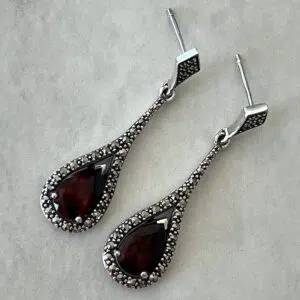 Boucles d'oreilles argent et grenat posées sur fond gris