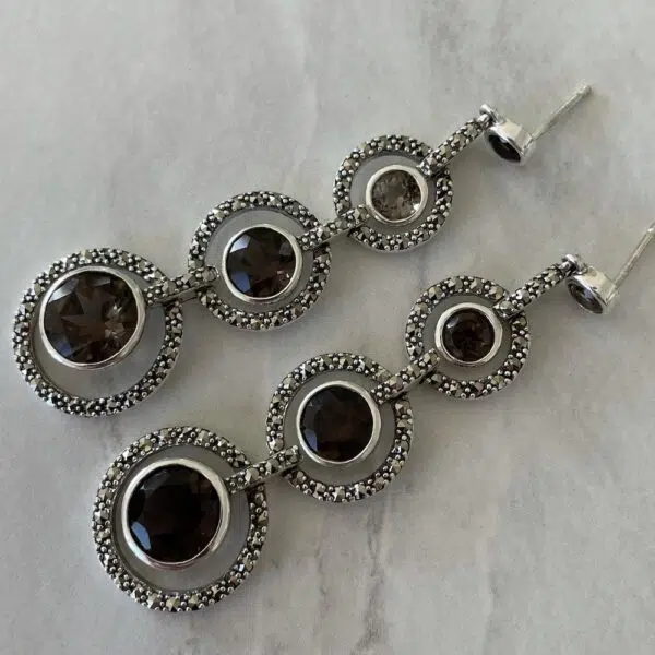Boucles d'oreilles pendantes avec trois pierres de quartz fumé posées sur une table blanche