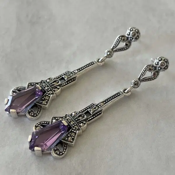 Vintage-style amethyst art deco earrings set on a gray background.