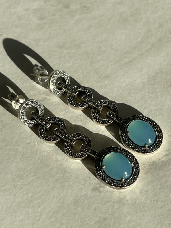 Boucles d'oreilles jade bleu vintage art déco pendantes posées sur fond gris.