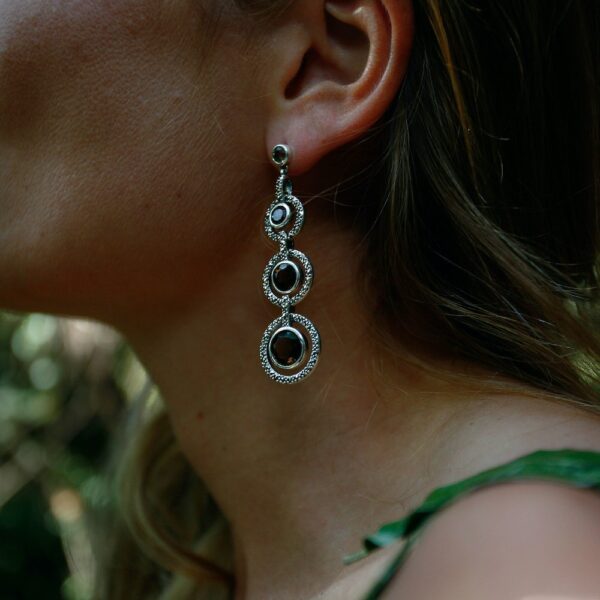 Boucles d'oreilles pendantes avec trois pierres de quartz fumé portées sur l'oreille gauche.