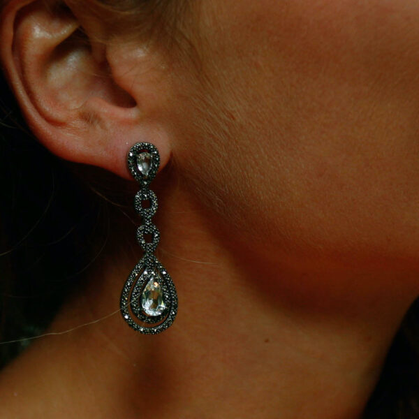 Boucles d'oreilles en argent pendantes sertis de topaze clair et de marcassite portées sur l'oreille droite.